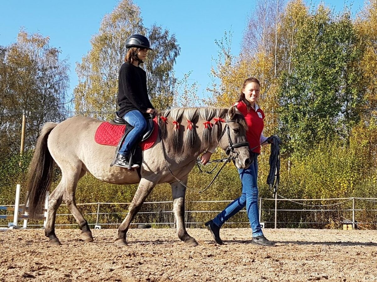 trenere Ieva Prūse ved pie pavadas jauno jātnieci zirga mugurā